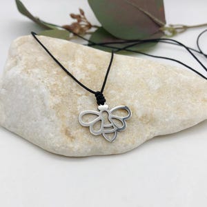May include: A silver bee pendant necklace on a black cord. The bee is a cutout design with a detailed body and wings.