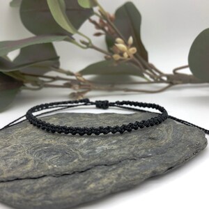 Puede incluir: Un brazalete trenzado negro con un dise&ntilde;o anudado. El brazalete est&aacute; sobre una roca gris.