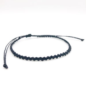 Puede incluir: Una sencilla pulsera trenzada negra con cierre anudado.