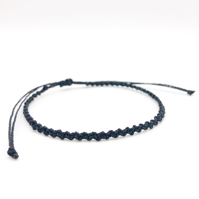 Puede incluir: Una sencilla pulsera trenzada negra con cierre anudado.