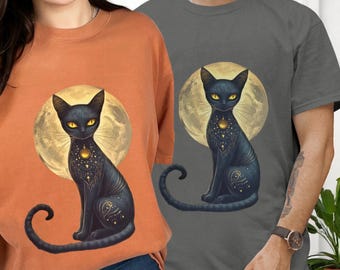 May include: Two t-shirts, one orange and one gray, each featuring a black cat design. The cat is set against a full moon, with yellow eyes and intricate golden details. The design is centered on the front of the shirts.