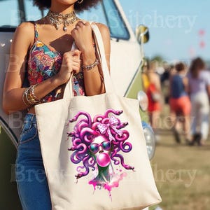 May include: A cream-colored tote bag featuring a vibrant illustration of Medusa with pink hair, sunglasses, and a bubblegum bubble. The Medusa graphic is surrounded by pink snakes and a pink bow. The bag is held by a person wearing a colorful top and blue jeans.