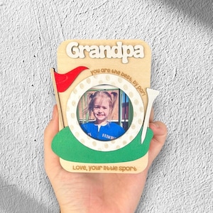 Op de afbeelding: Houten fotolijst met een golf thema. De lijst heeft een foto van een jong meisje in het midden. De lijst zegt "Grandpa you are the best, by par! Love, your little sport".