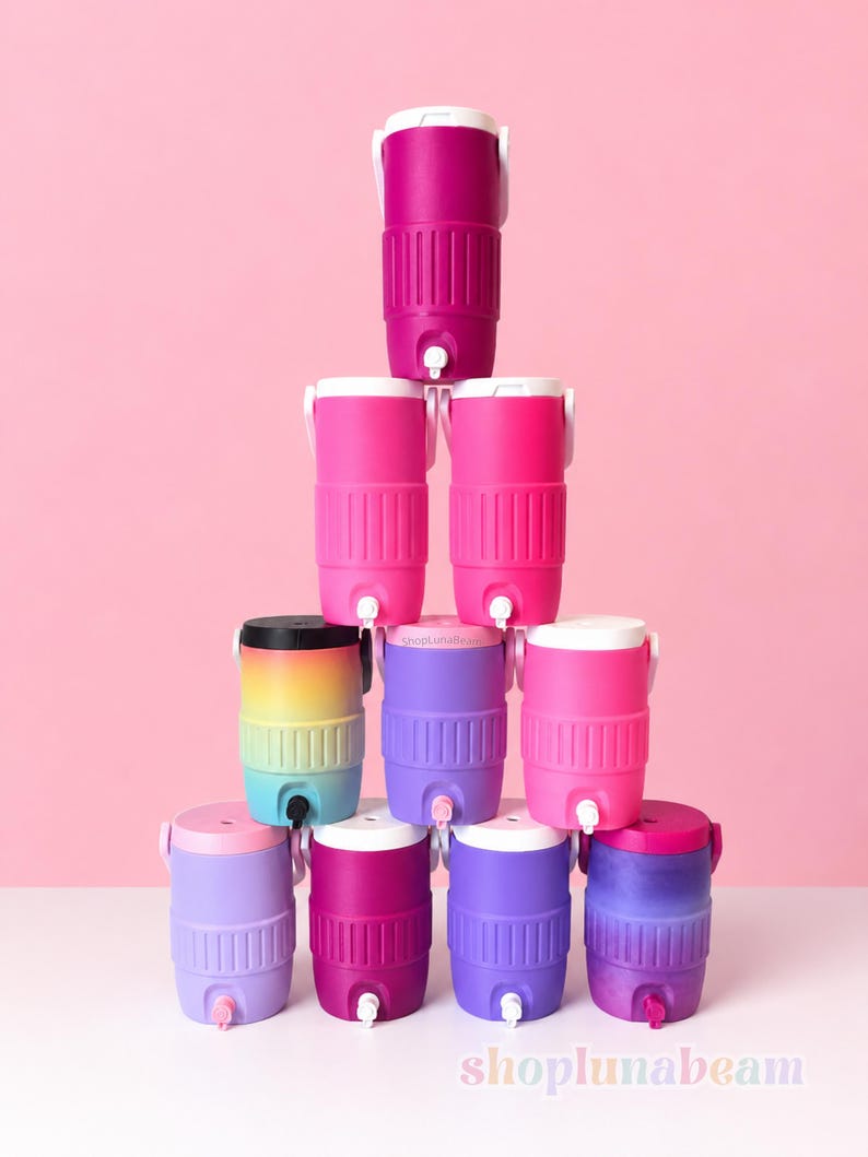 May include: A collection of brightly coloured beverage coolers in shades of pink, purple, and a rainbow gradient. Each cooler has a white lid, a spigot, and a handle. The coolers are arranged against a pink background.