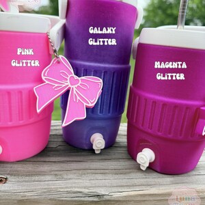 May include: Three brightly coloured glitter coolers in pink, purple, and magenta. Each cooler has a white lid and a silver straw. The purple cooler is labelled "Galaxy Glitter," the pink cooler is labelled "Pink Glitter," and the magenta cooler is labelled "Magenta Glitter."