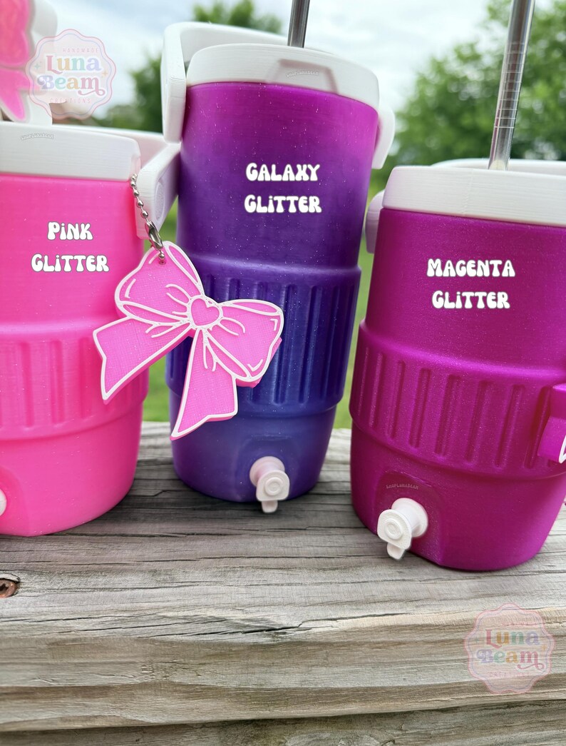 May include: Three brightly coloured glitter coolers in pink, purple, and magenta. Each cooler has a white lid and a silver straw. The purple cooler is labelled "Galaxy Glitter," the pink cooler is labelled "Pink Glitter," and the magenta cooler is labelled "Magenta Glitter."