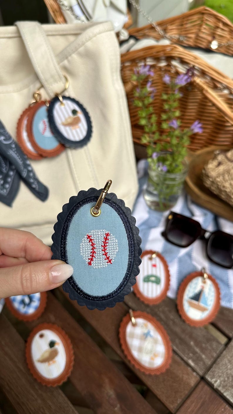 K&ouml;nnte beinhalten: Ovale Schl&uuml;sselanh&auml;nger mit verschiedenen Designs, darunter ein Baseball, ein Segelboot und eine Ente. Der Baseball-Schl&uuml;sselanh&auml;nger ist hellblau mit einem roten Baseball-Naht-Design. Andere Schl&uuml;sselanh&auml;nger haben braune, gewellte R&auml;nder.