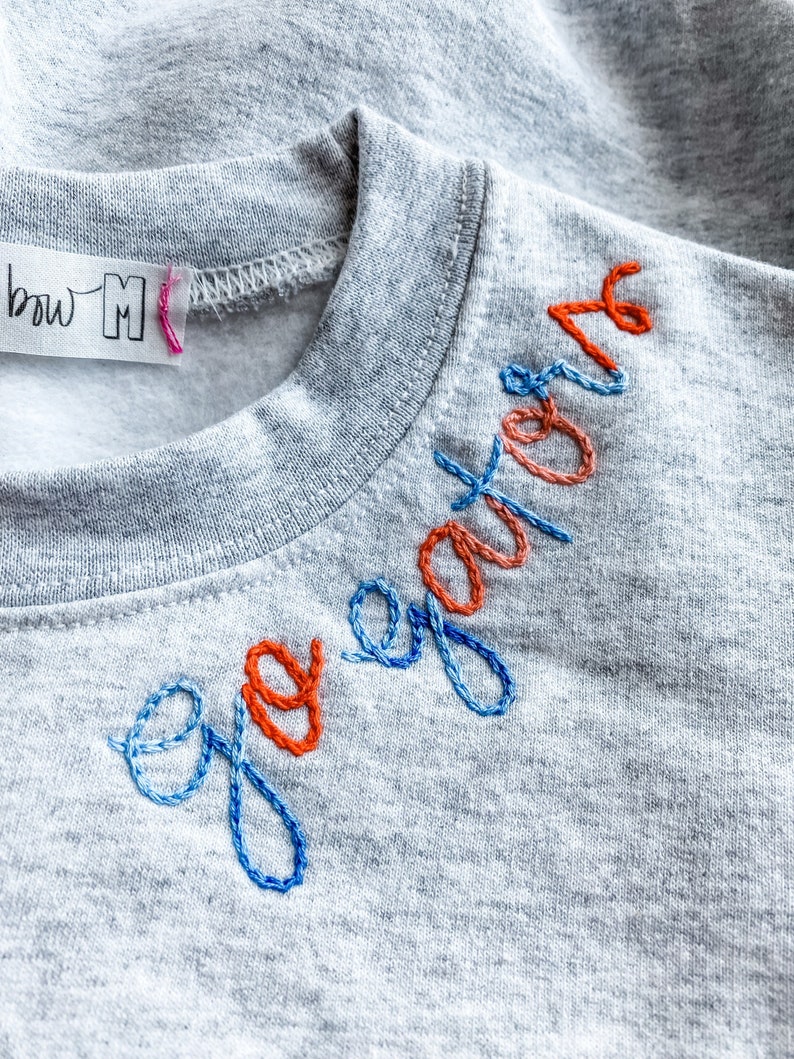 May include: A gray sweatshirt with the word "ego" embroidered in blue and orange thread.