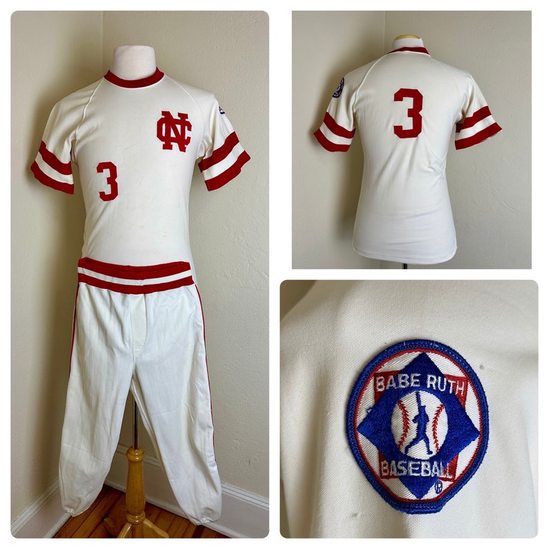 May include: Vintage baseball uniform in cream with red accents. The jersey features the number 3, the letters "NC", and red stripes on the sleeves. The pants are white with red side stripes. A "Babe Ruth Baseball" patch is visible.