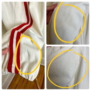 May include: Cream-colored athletic jacket with red and white stripes down the sleeves. The jacket has a ribbed cuff and a drawstring hem. There are some stains on the jacket.