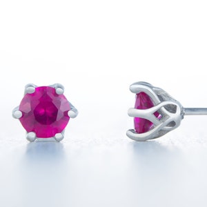 Peut inclure: Une paire de boucles d'oreilles en argent avec une pierre précieuse en rubis dans chaque boucle. Le rubis est de couleur rouge foncé et est serti dans un cadre en argent.