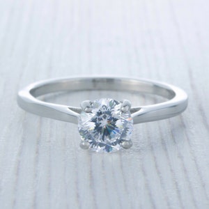 Könnte beinhalten: Ein silberner Verlobungsring mit einem runden, klaren Diamanten.