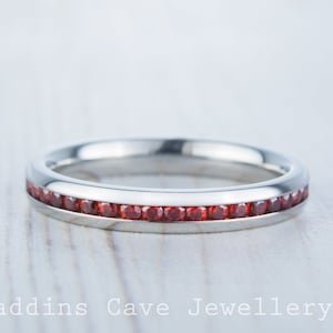 Può includere: Un anello a fascia d'argento con una fila di piccole pietre preziose rosse incastonate nella fascia.