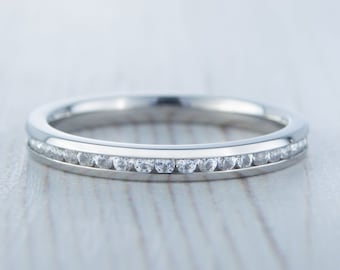 May include: A thin silver band with a row of small diamonds set in a channel setting.