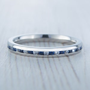 May include: A thin silver band with a row of small blue sapphires and white diamonds set in a channel setting.