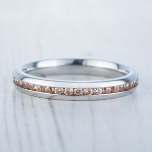 Peut inclure: Une bague en argent avec une rangée de petites pierres précieuses brun clair serties au centre.