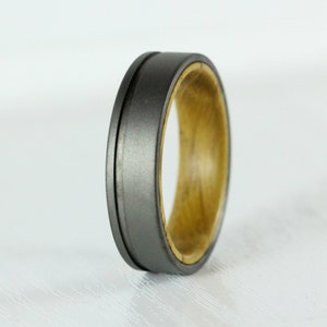 Puede incluir: Un anillo gris y madera con un borde biselado. El anillo est&aacute; hecho de titanio y madera.