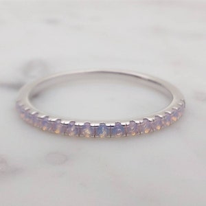 May include: A delicate silver band ring with a row of small, clear opal stones.