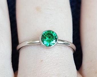 May include: A silver ring with a green gemstone. The ring is on a person's finger.