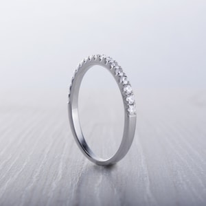 May include: A silver band ring with a row of small, clear gemstones set along the top. The ring is displayed on a light gray surface, with the focus on the sparkling stones and the polished metal.