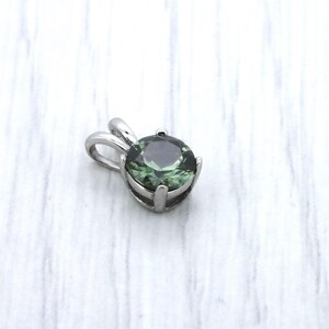 May include: A silver pendant featuring a round, dark green gemstone.