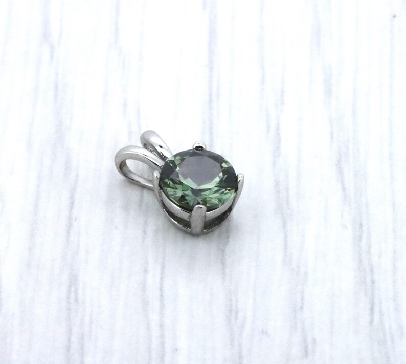 May include: A silver pendant featuring a round, dark green gemstone.