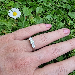 May include: A silver ring with three round clear stones set in a curved row.