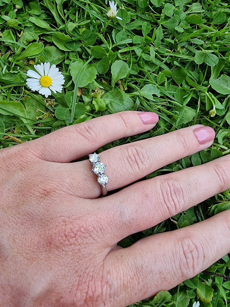 May include: A silver ring with three round clear stones set in a curved row.