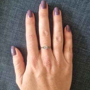 May include: A silver ring with a large, round, clear gemstone surrounded by smaller green gemstones. The ring is on a person's finger.