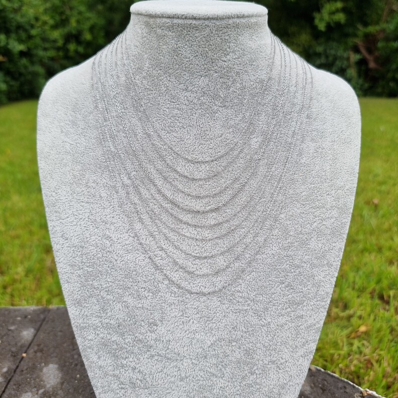 May include: A set of silver chain necklaces of varying lengths, displayed on a white mannequin bust.