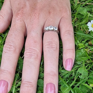 May include: A silver ring with four clear round stones set in a row. The ring is on a finger with pink nail polish.