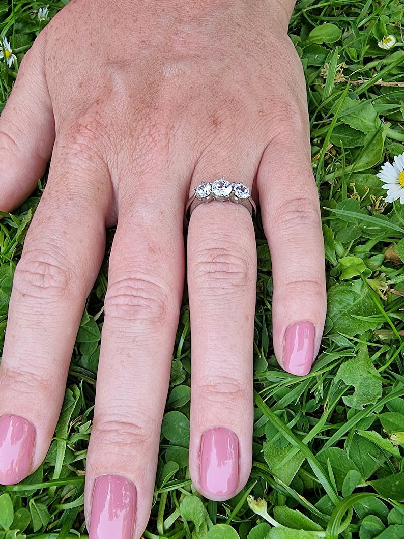 May include: A silver ring with four clear round stones set in a row. The ring is on a finger with pink nail polish.
