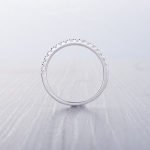 May include: A silver ring with a band of small, evenly spaced gemstones. The ring is set against a light, neutral background, highlighting its polished surface and the sparkle of the stones. The ring is a jewelry item.