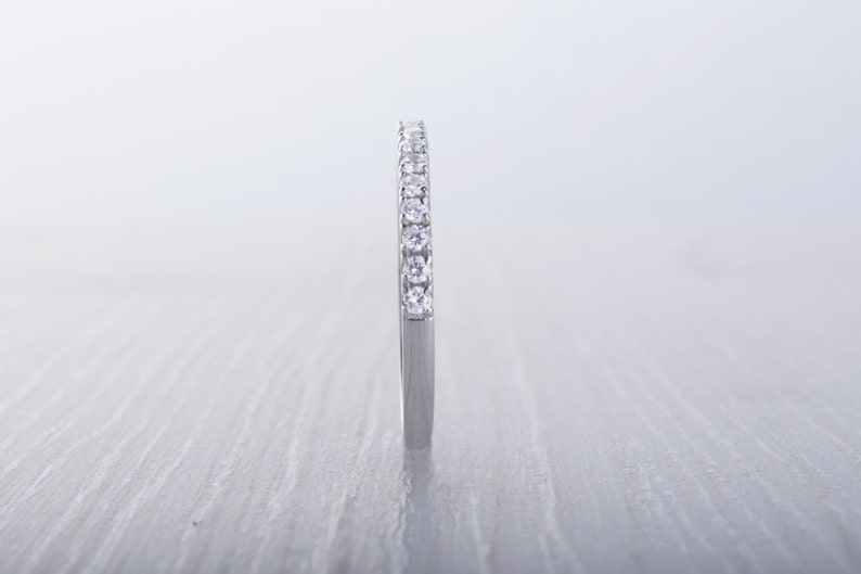 May include: A silver band ring with a row of small, clear gemstones set across the top. The ring is shown against a light, textured background, highlighting the sparkle of the stones.
