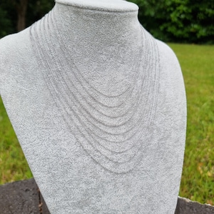 May include: A silver chain necklace with multiple strands layered on a white mannequin bust. The necklace is made of a delicate chain link design.