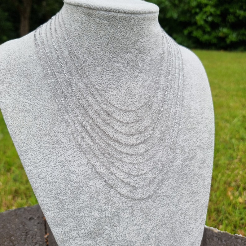 May include: A silver chain necklace with multiple strands layered on a white mannequin bust. The necklace is made of a delicate chain link design.