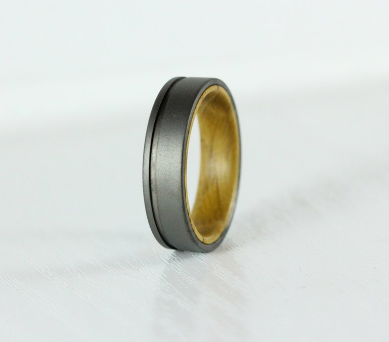 Puede incluir: Un anillo gris y madera con un borde biselado. El anillo est&aacute; hecho de titanio y madera.