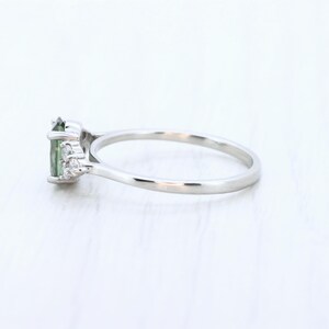 May include: A silver ring featuring a green oval-cut gemstone and small, clear accent stones. The ring has a delicate band and a classic, elegant design, perfect for everyday wear or special occasions.