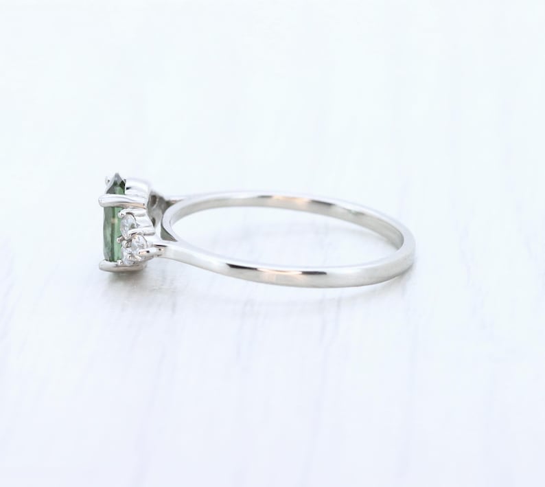 May include: A silver ring featuring a green oval-cut gemstone and small, clear accent stones. The ring has a delicate band and a classic, elegant design, perfect for everyday wear or special occasions.