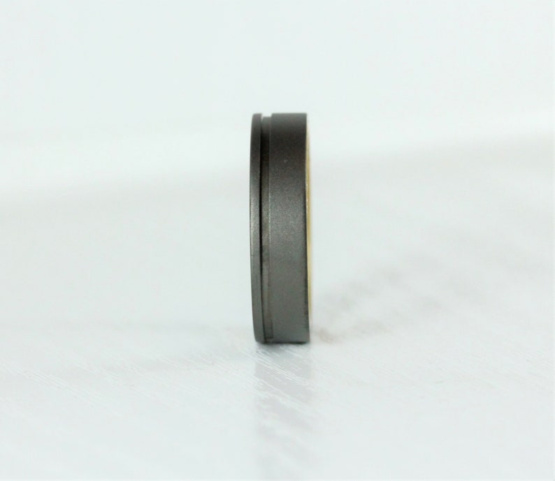 Puede incluir: Un anillo de metal gris con un borde biselado y un acabado liso.