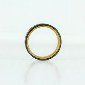 Puede incluir: Un anillo negro y dorado con una incrustaci&oacute;n de madera. El anillo es de metal y tiene un acabado pulido.