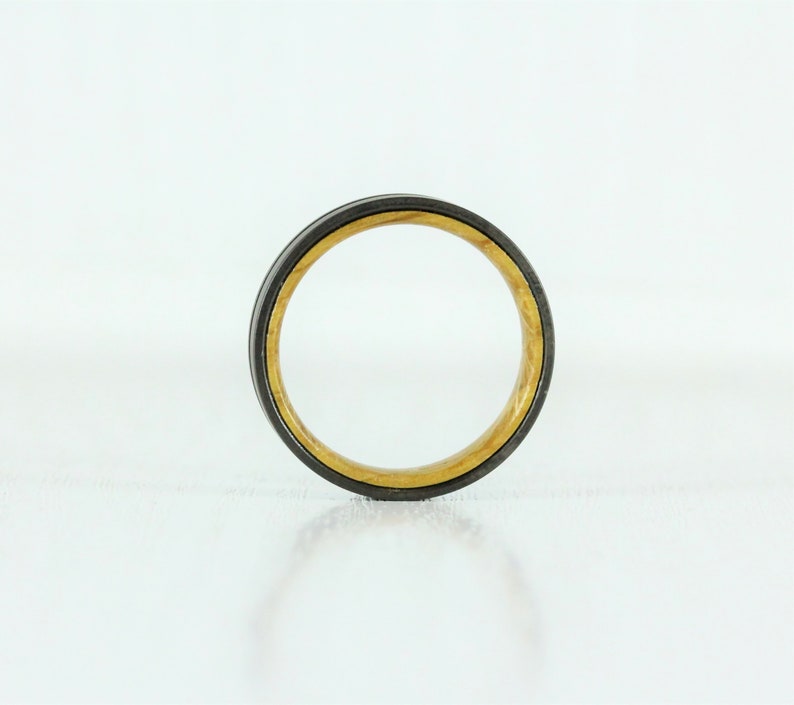 Puede incluir: Un anillo negro y dorado con una incrustaci&oacute;n de madera. El anillo es de metal y tiene un acabado pulido.