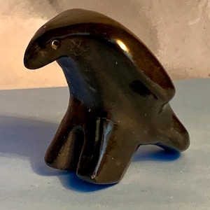 May include: A glossy, dark brown sculpture of a stylized bird. The bird has a curved beak and a smooth, rounded body. The sculpture is perched on a flat base and appears to be made of a solid, polished material.