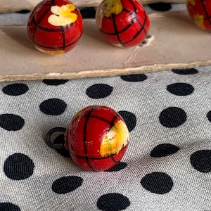 May include: Six red and yellow globe-shaped buttons with black lines and a white flower design. The buttons are on a white card with black polka dots.