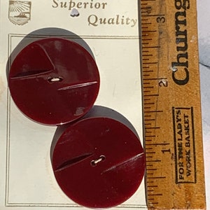 May include: Two large, dark red, plastic buttons with a single hole in the center. The buttons have a slightly raised design on the surface. The buttons are on a white card with the text "Superior Quality" and "CZECHOSLOVAKIA".