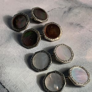 May include: A collection of six vintage cufflinks. Each cufflink features an octagonal design with a silver-toned metal frame. The center of each cufflink has a different iridescent or pearlescent finish, including brown, green, and white.