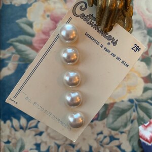 May include: A card of six pearlescent buttons from Costumakers, size 22/9/10, with the text "GUARANTEED TO WASH AND DRY CLEAN". The card is held by a gold-coloured hand. The price is 29¢. Made in Japan.