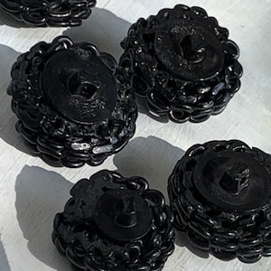 May include: Four black buttons with a decorative chain-like design around the edge. The buttons are round and have a flat back.