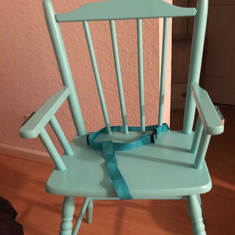Puede incluir: Una silla de madera de color turquesa claro con un respaldo alto de barrotes verticales, dos reposabrazos y un asiento plano. Una correa de seguridad de nailon turquesa a juego con una hebilla de pl&aacute;stico negra est&aacute; sujeta al asiento.