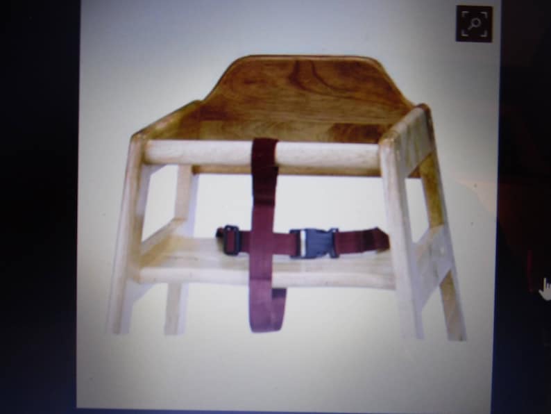 Puede incluir: Una trona de madera de color claro con un acabado de veta natural suave. La silla incluye un respaldo resistente, reposabrazos laterales y una barra de seguridad frontal. Una correa de nailon color granate oscuro con hebilla de pl&aacute;stico negro.